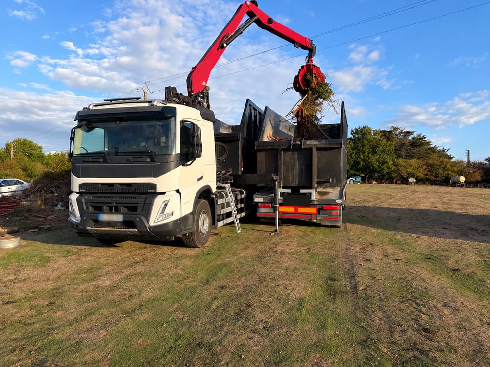 Une grue à grappin charge des déchets verts dans une benne